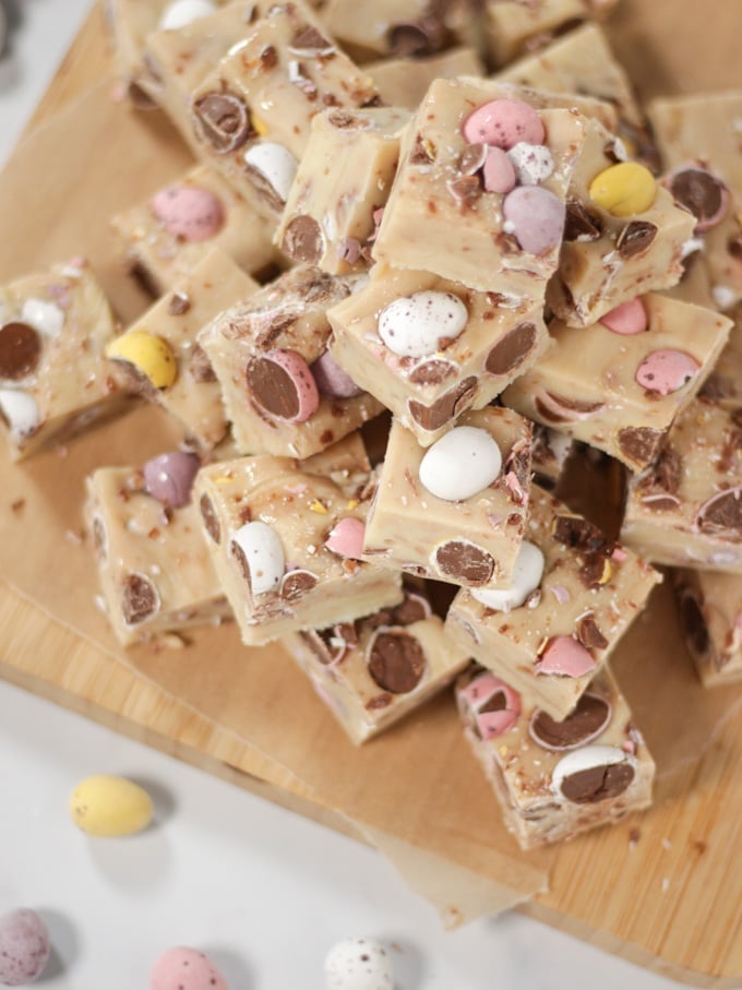 Pile of cubes of mini egg fudge on a wooden board.