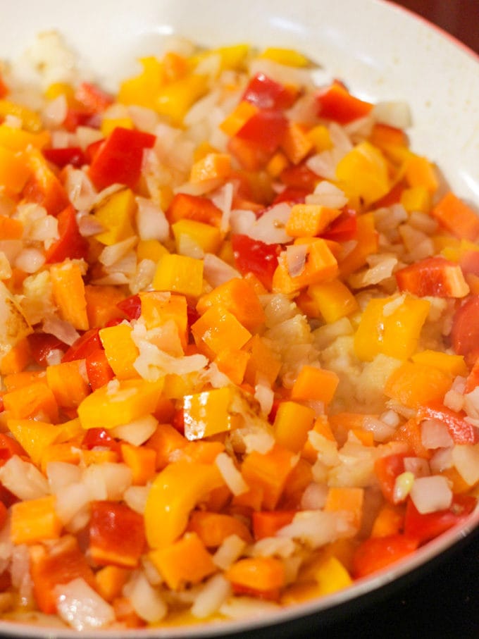 Fried cubes of red pepper, orange pepper, and onion fried in a pan. Egg Fried Rice recipe.