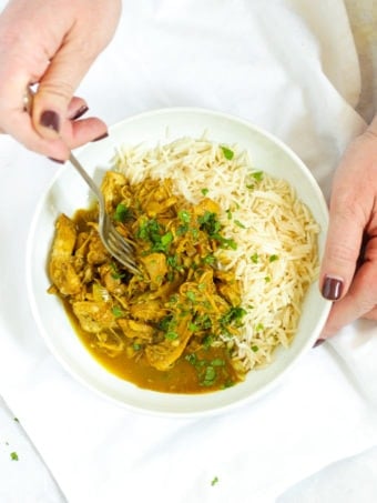 Hands holding a bowl of healthy slow cooker chicken curry with rice