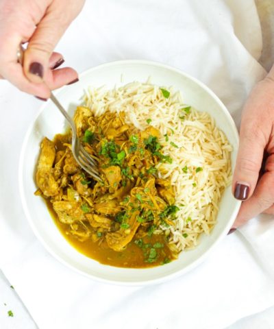 Hands holding a bowl of healthy slow cooker chicken curry with rice