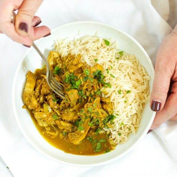 Hands holding a bowl of healthy slow cooker chicken curry with rice