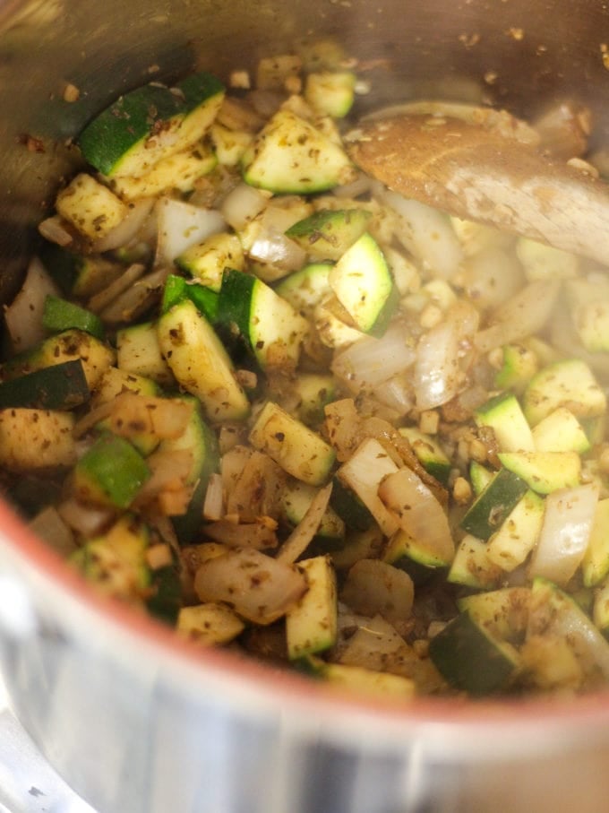 Courgette pieces frying with onions and garlic in a saucepan. Step 1 in the recipe for Vegetarian Moussaka.