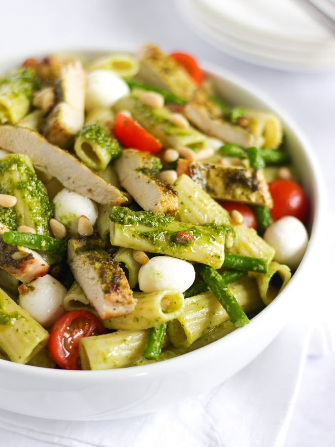 Chicken pesto pasta bake with tomatoes and green beans in a white bowl