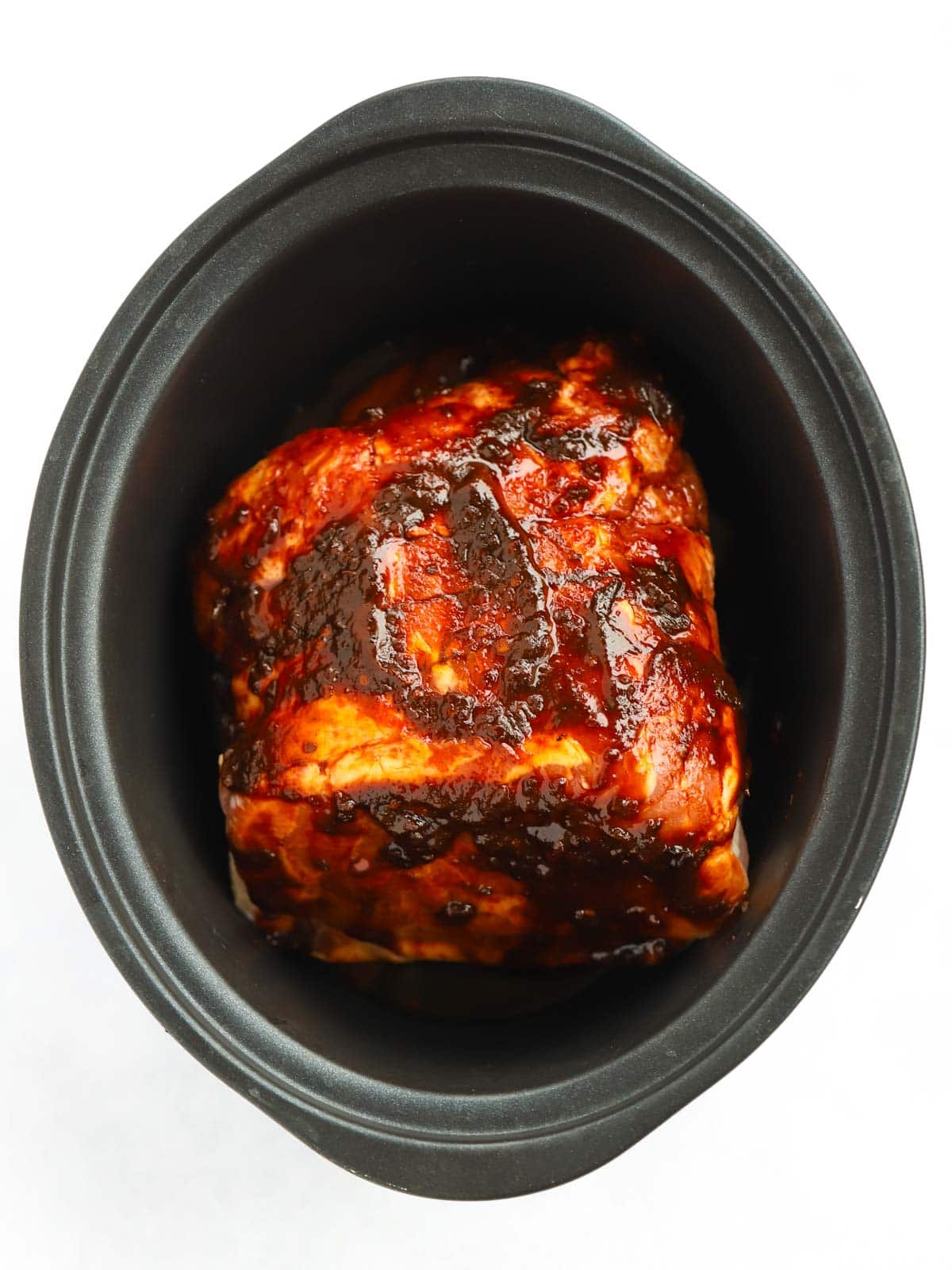 pork shoulder joint smothered in chipotle, ketchup and honey marinade sat in a black slow cooker