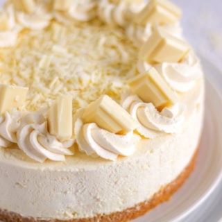 White chocolate cheesecake on a plate with cream and chunks of white chocolate on top