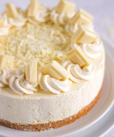 White chocolate cheesecake on a plate with cream and chunks of white chocolate on top