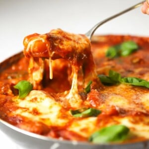 Baked gnocchi topped with mozzarella cheese and basil being lifted from the pan