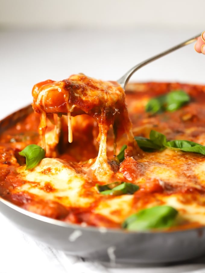 Baked gnocchi topped with mozzarella cheese and basil being lifted from the pan