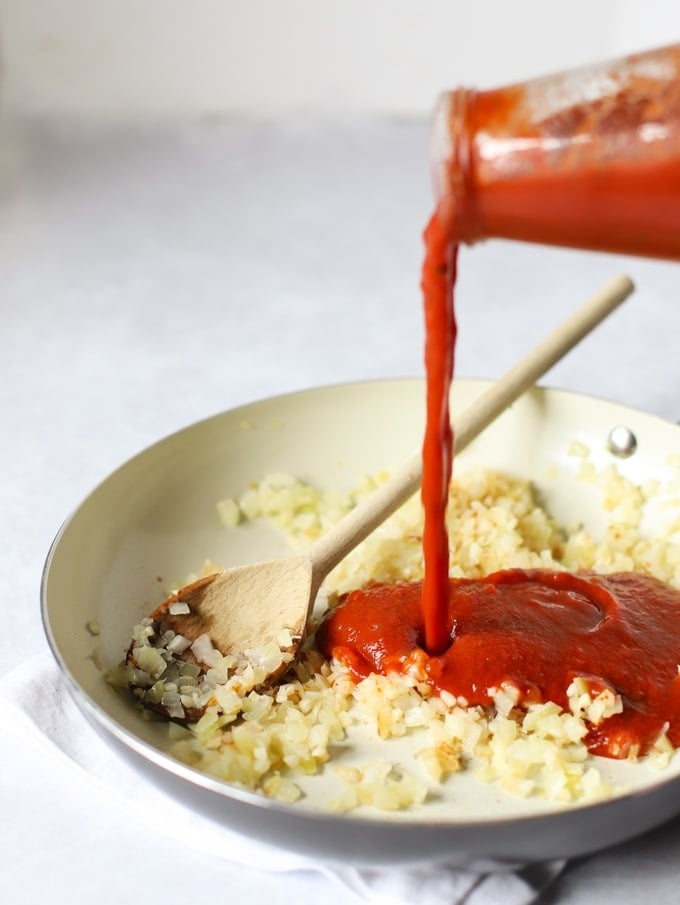 Fried onions in a frying pan with passata being poured in.