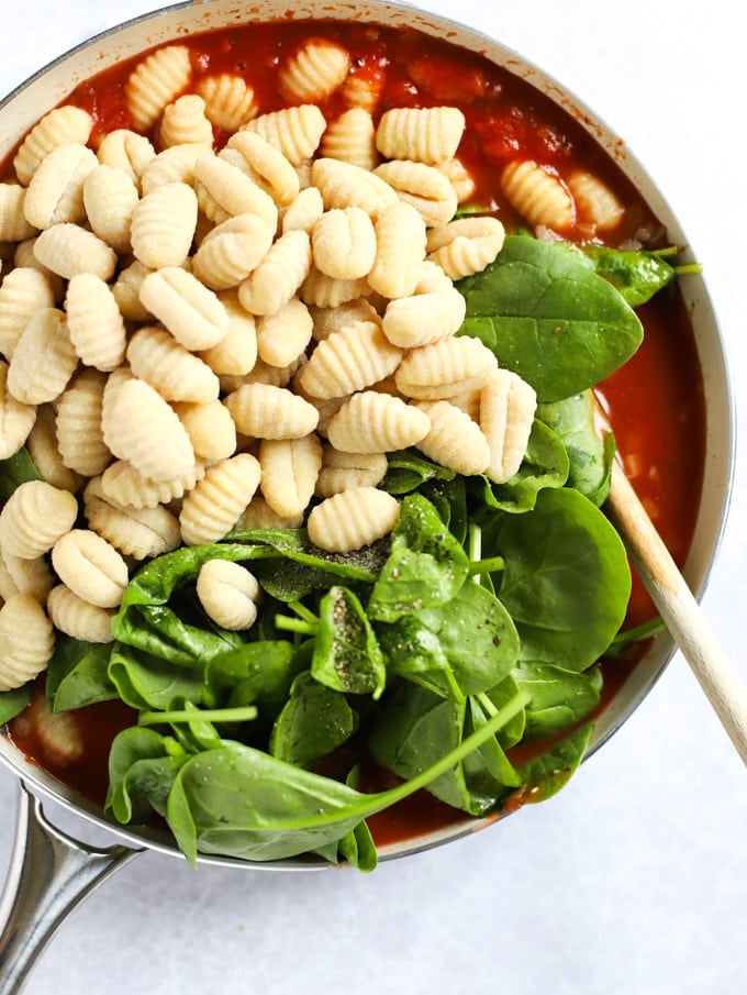 Spinach and potato dumplings being added to a pan of tomato sauce