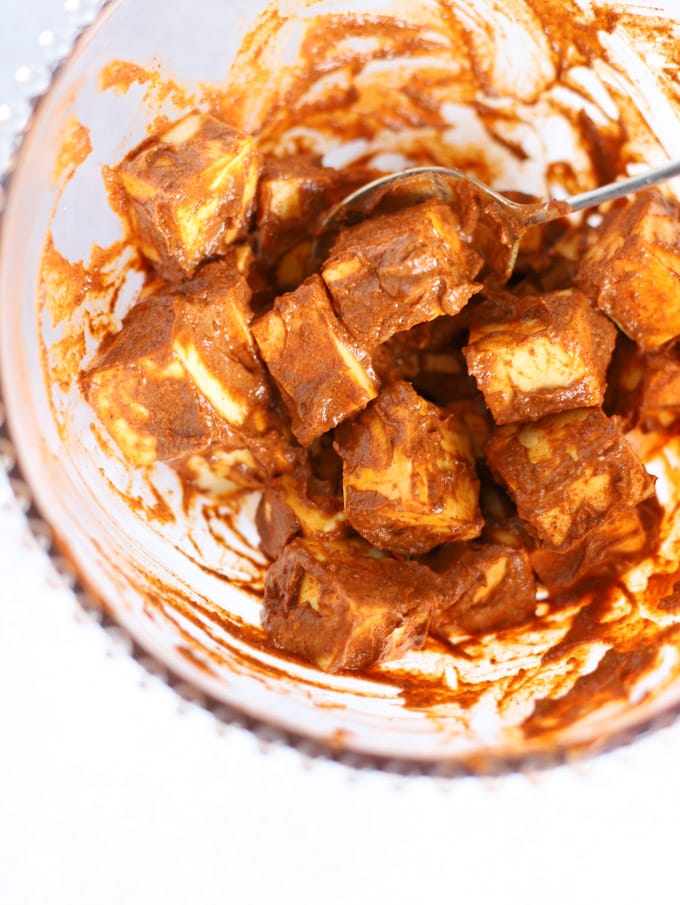 Cubes of Indian cheese coated in spices and yoghurt in a bowl.