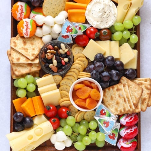 Cheese platter for kids with grapes, crackers, nuts and tomatoes on a board