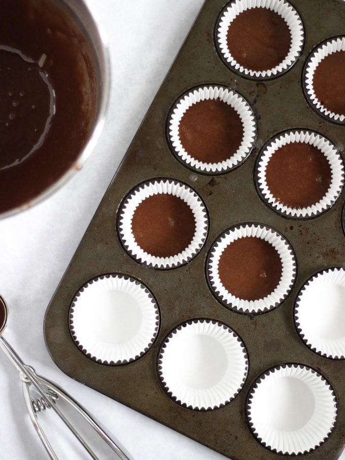 Chocolate cupcakes scooped into a muffin tin ready to be baked.