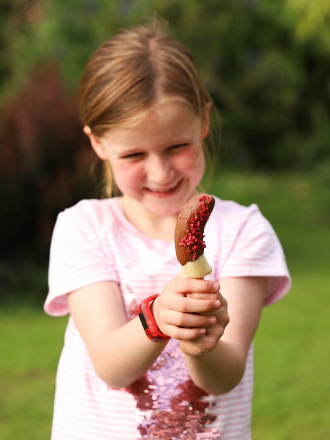 Girl holding homemade lolly with sprinkles and garden in background