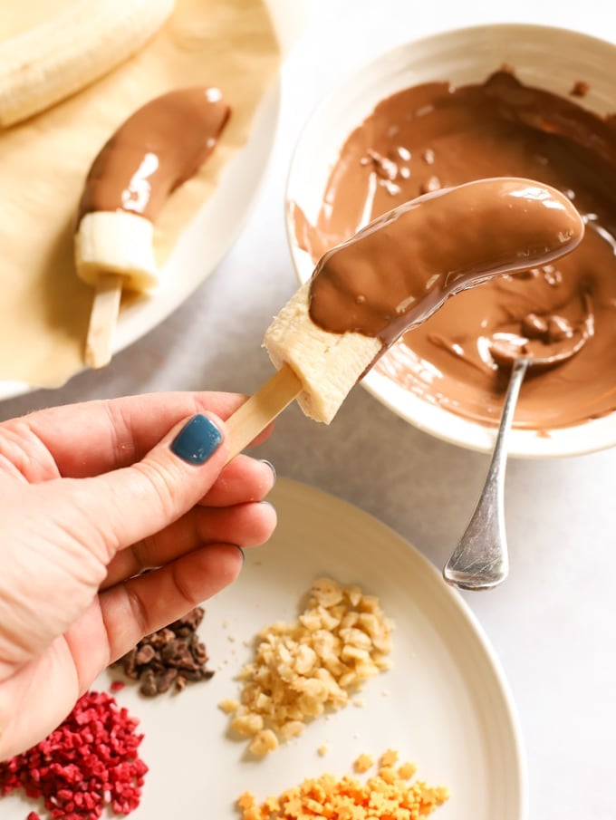 Banana dipped in chocolate ready to be frozen with sprinkles