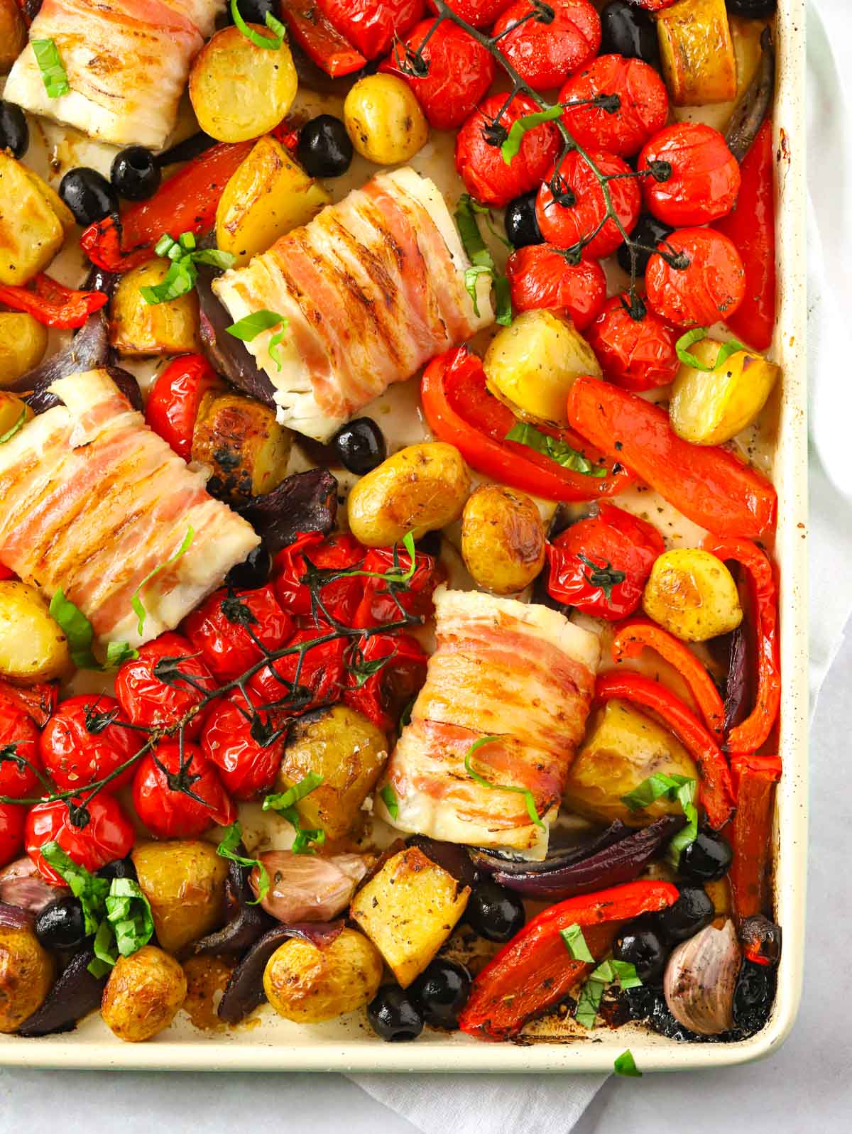 A baking tray with cod wrapped in bacon and vegetables cooked.