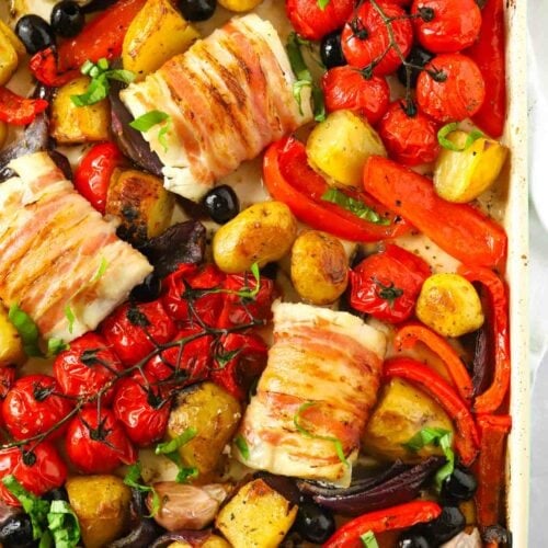 A baking tray with cod wrapped in bacon and vegetables cooked.