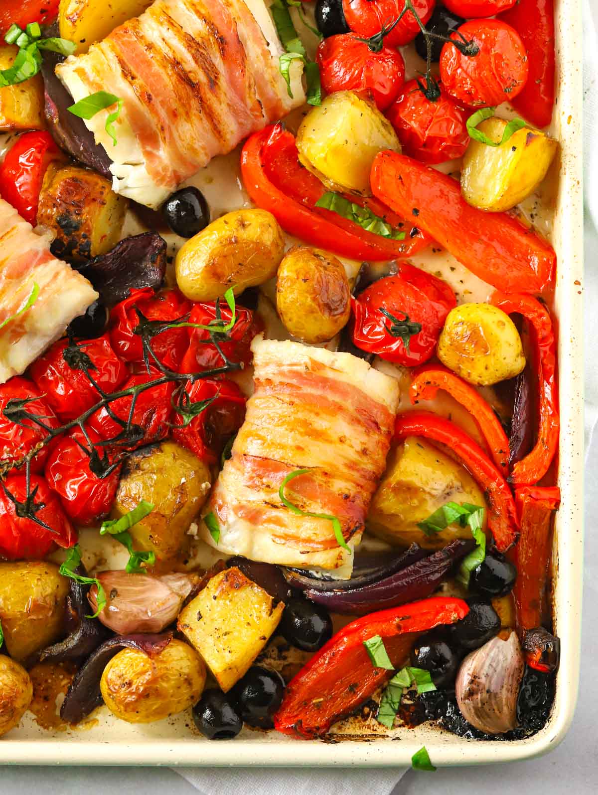 Baked cod pieces with Italian style vegetables on a tray.