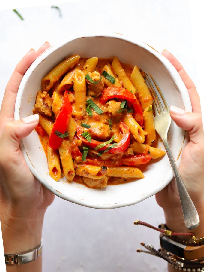 Hands holding a bowl of easy one post creamy sausage pasta recipe.