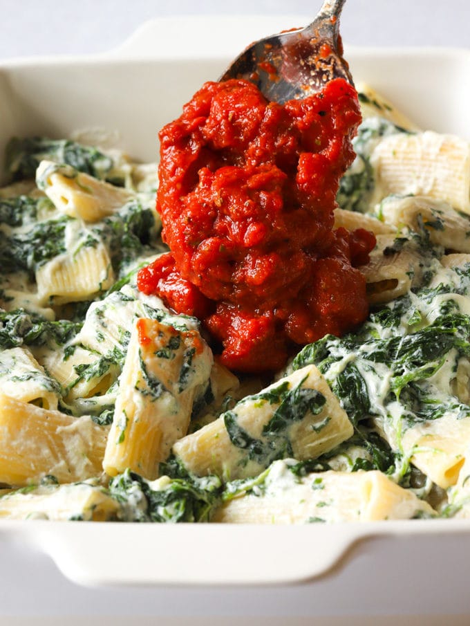 Pasta with spinach and ricotta being topped with easy tomato sauce ready to be baked.