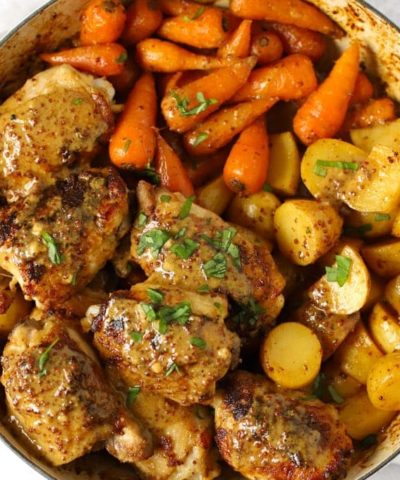 A large pan of chicken with carrots and potatoes to make up a tray bake of Honey Mustard Chicken recipe.