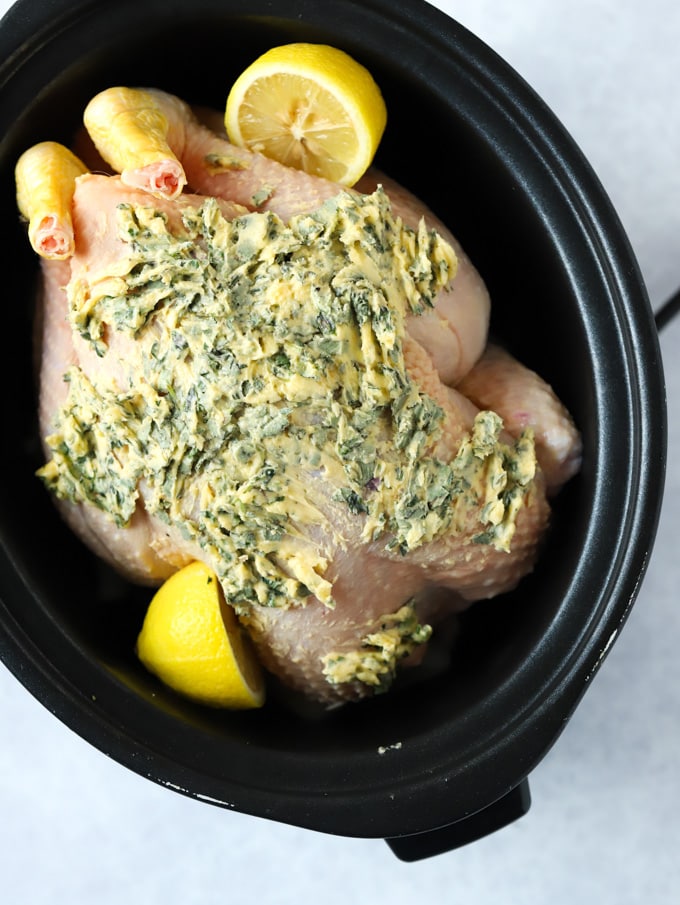 Whole chicken in slow cooker raw with herb butter and lemons.