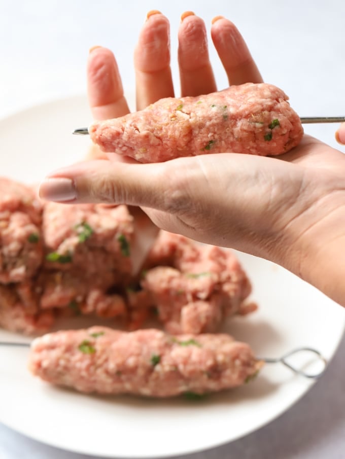 Shaping meat mince koftas onto metal skewer with hands