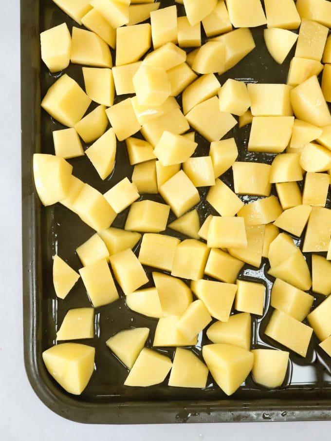 Cubes of potatoes on a baking tray, drizzled with oil and ready for the oven for step 1 in the recipe for parmentier potatoes.