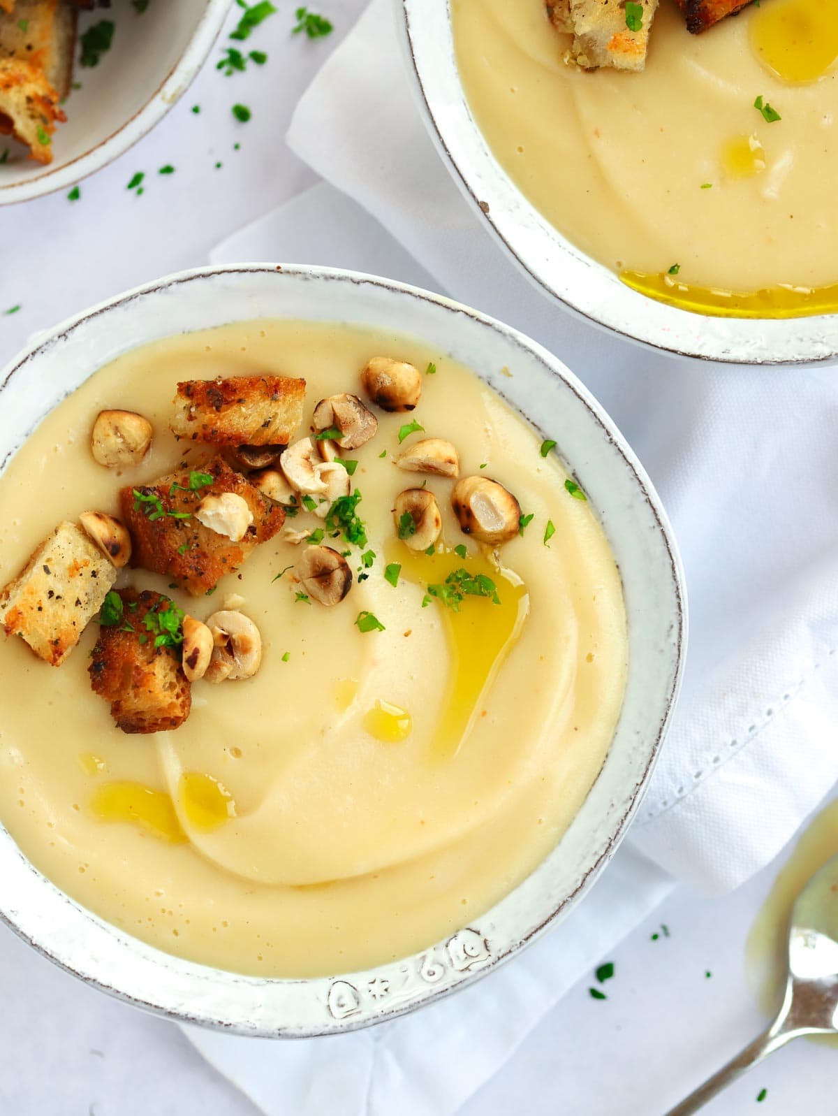 A bowl of parsnip soup on a white tablecloth with croutons.