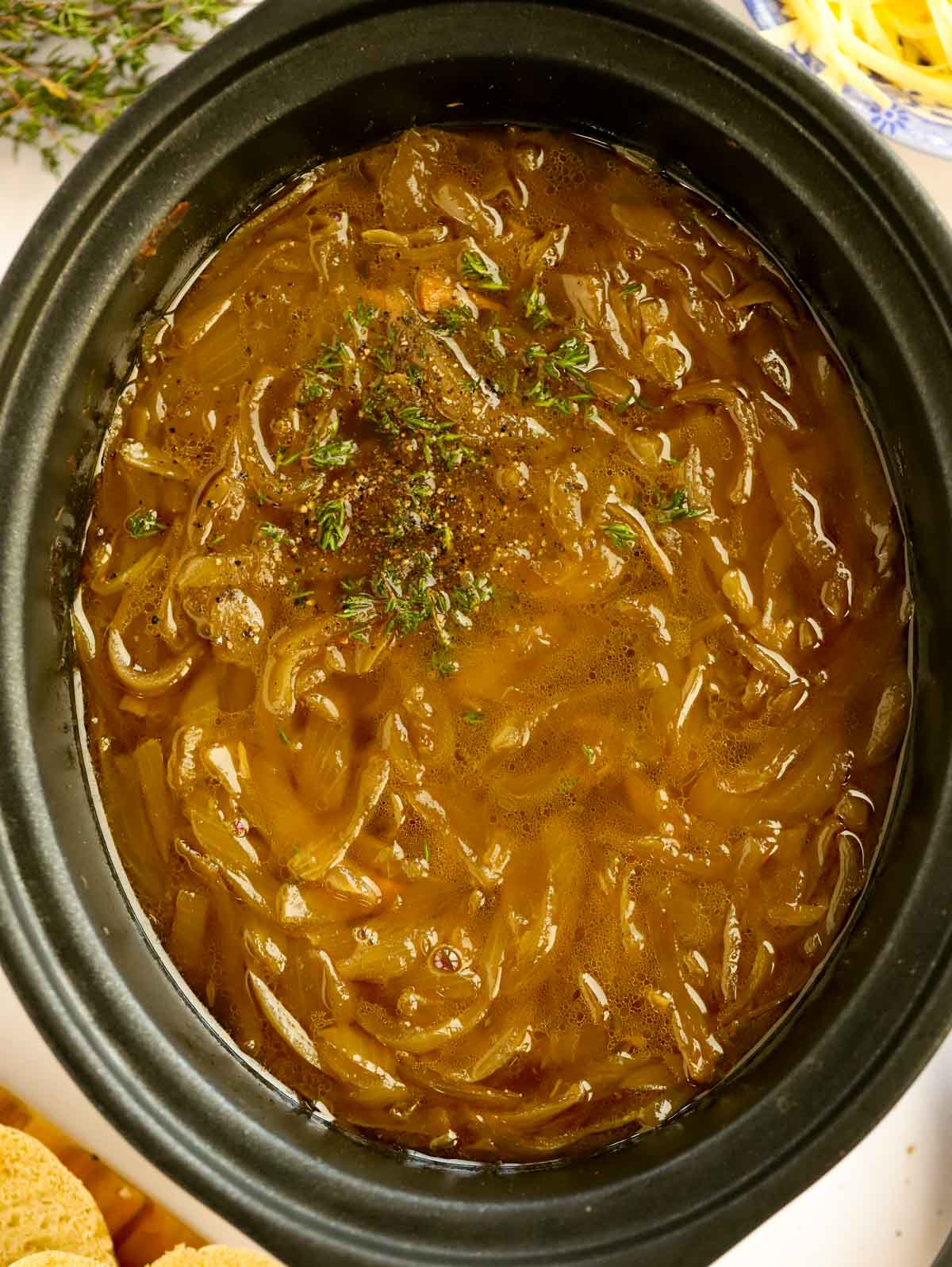 french onion soup topped with thyme in a black slow cooker