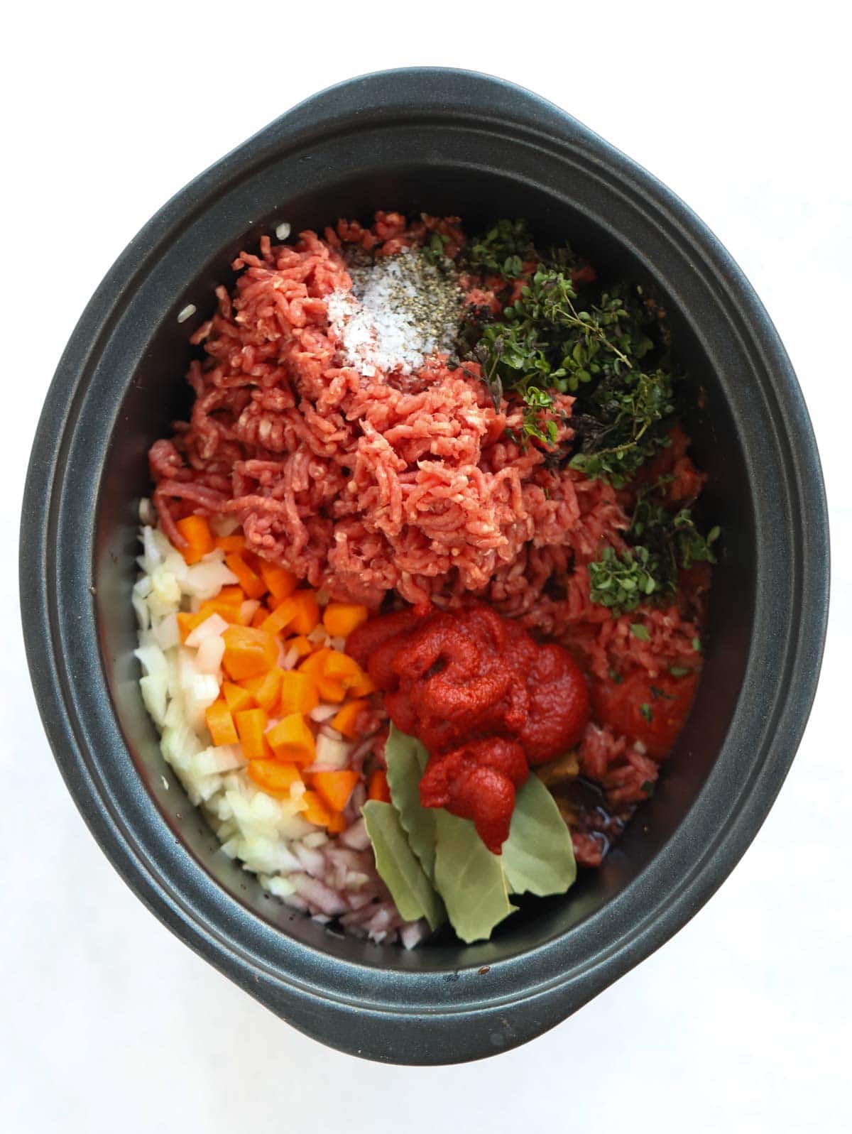 Raw ingredients in a slow cooker for beef bolognese.