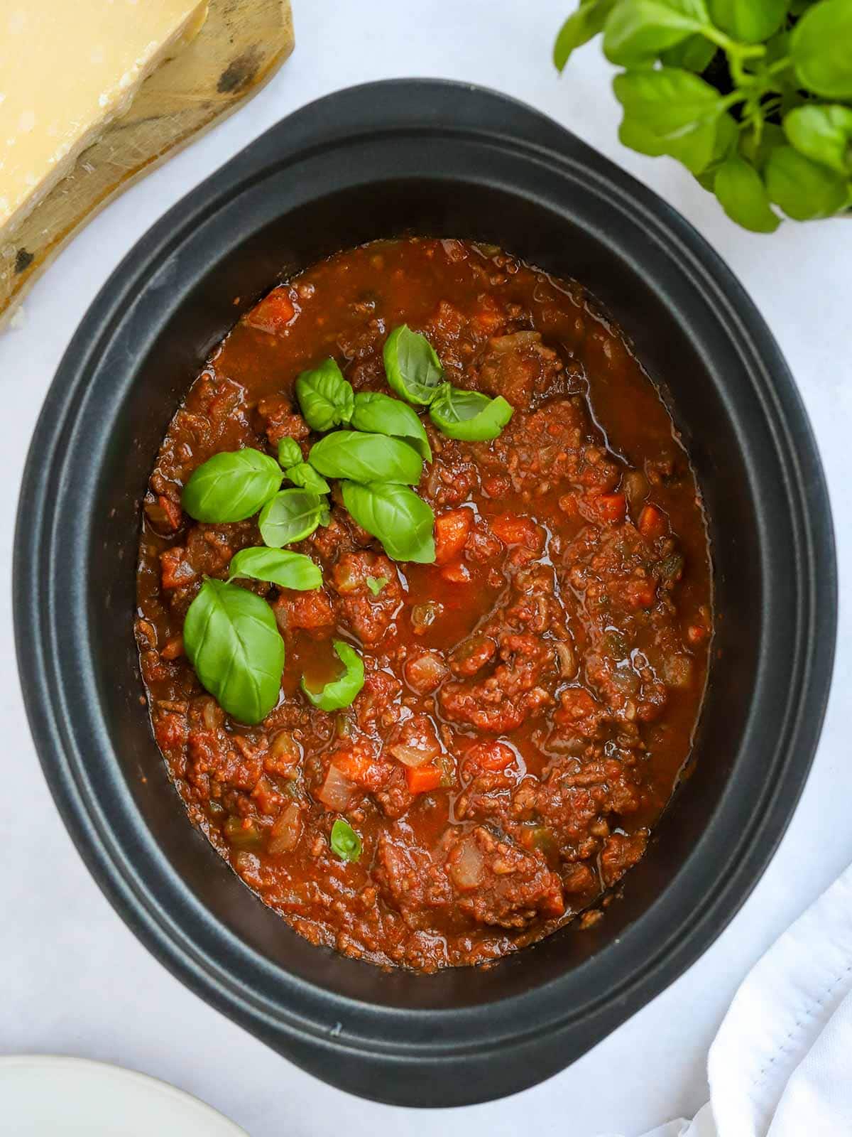 Slow cooker beef bolognese cooked in a crock pot, with basil on top.