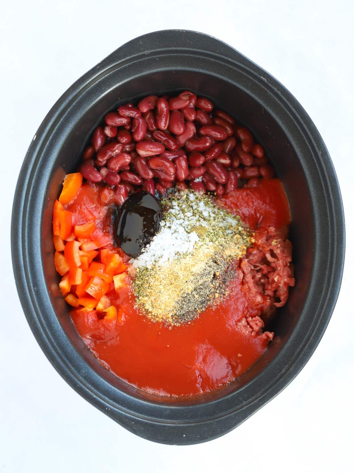 Raw ingredients for beef enchiladas in a slow cooker pan, ready to be cooked.