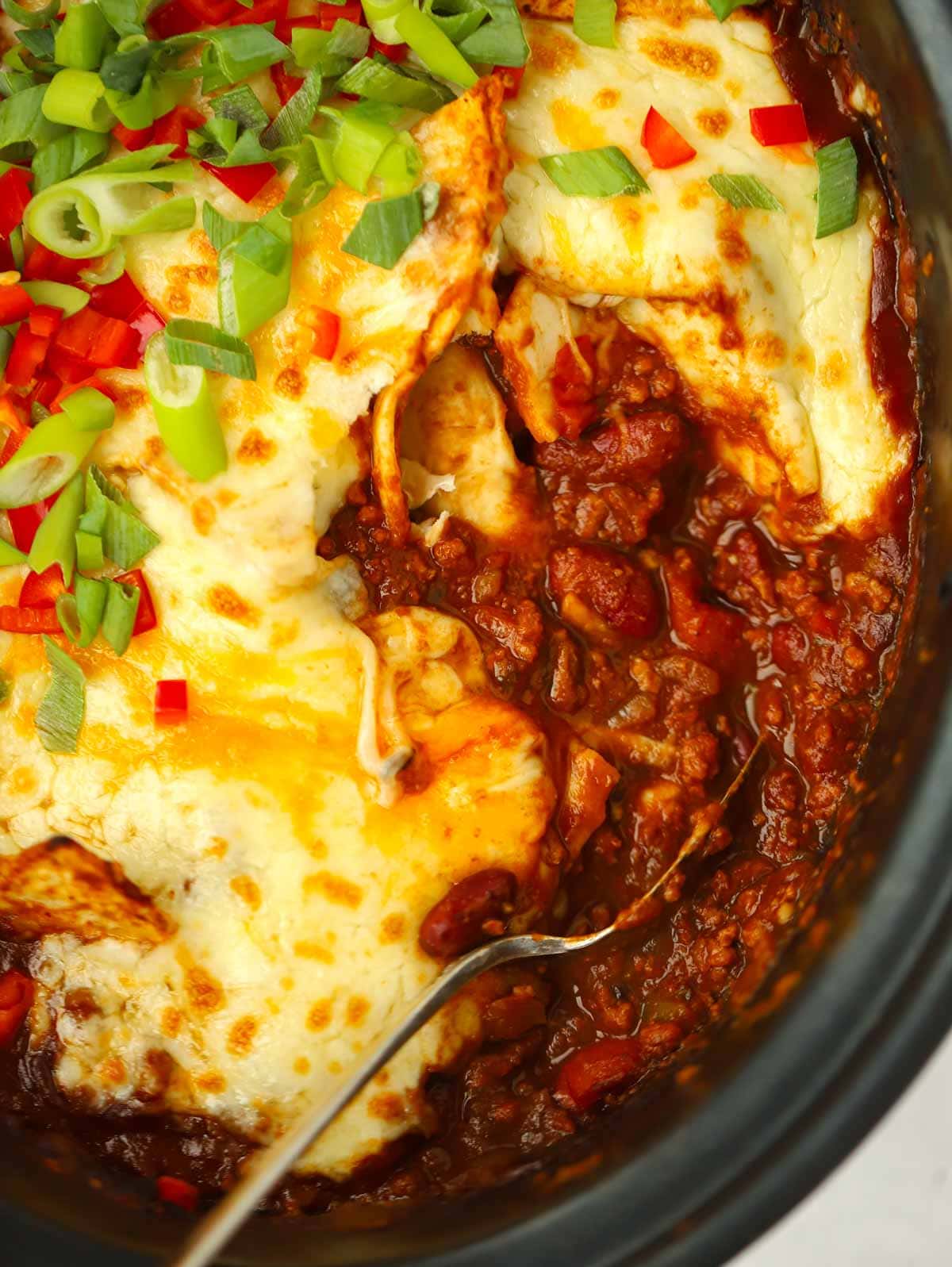 A close up on a spoon about to serve a portion of slow cooker beef enchiladas.