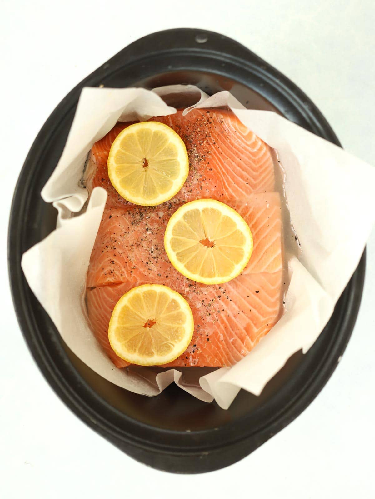 Raw salmon fillets in a slow cooker with lemon on top for the recipe Slow Cooker Salmon.