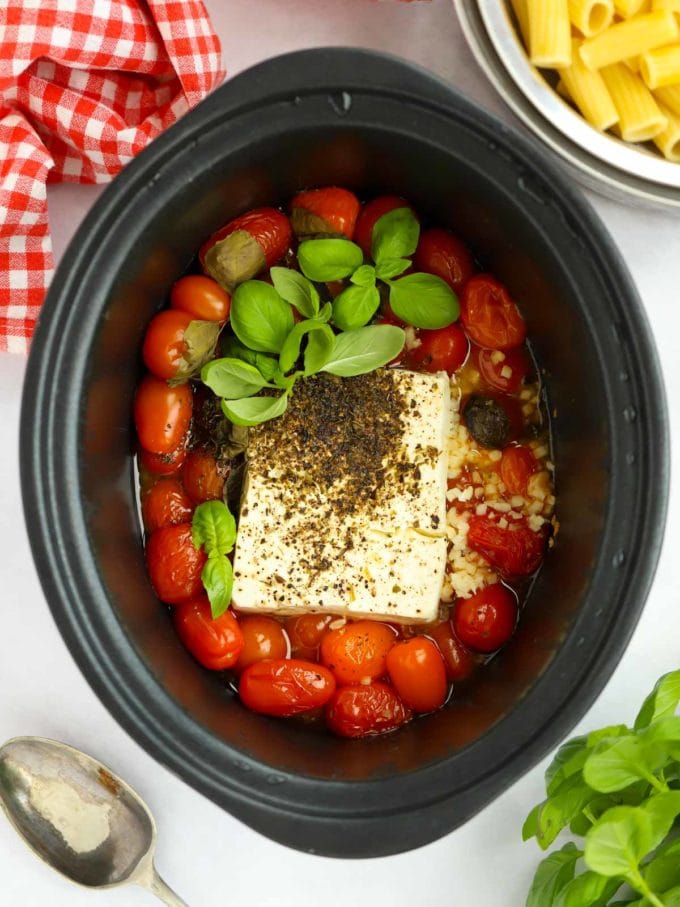 A slow cooker filled with cherry tomatoes and feta cheese, ready to cook.