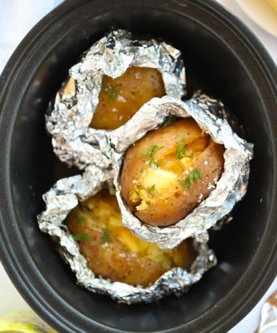 Jacket potatoes half covered in foil inside a slow cooker.