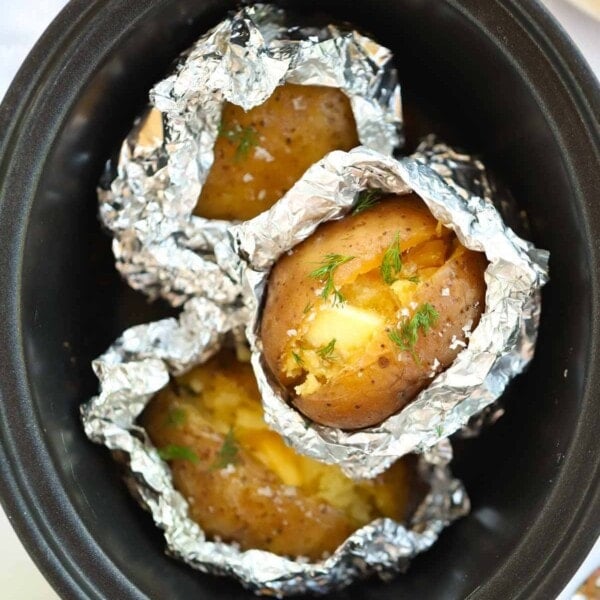 Jacket potatoes half covered in foil inside a slow cooker.