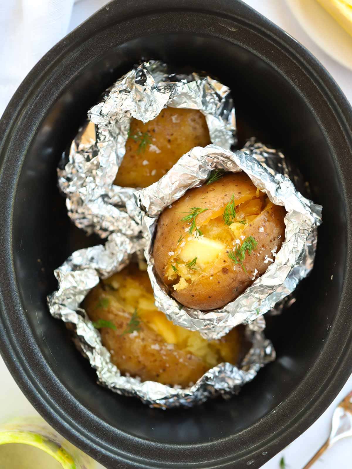 Jacket potatoes half covered in foil inside a slow cooker.