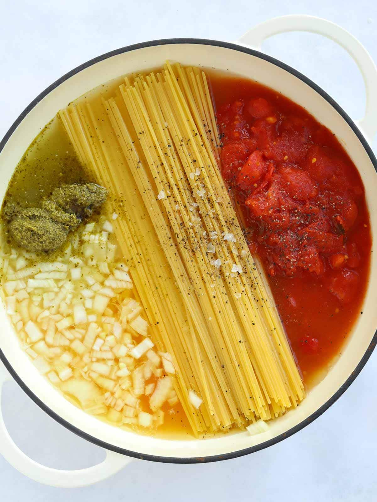 Ingredients for One Pot Pasta with Tomato Sauce all in the pan. Spaghetti, onion, tomato and pesto ready to be cooked.