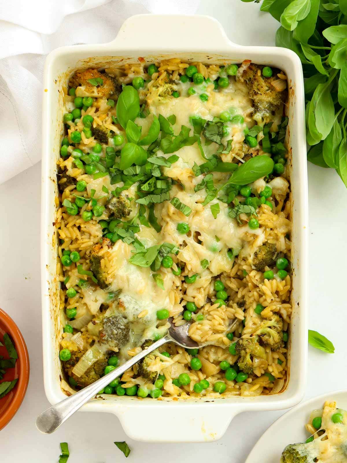 Oven dish filled with broccoli orzo pasta bake topped with cheese