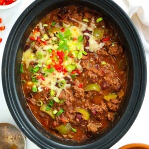 Slow cooker Chilli Con Carne topped with cheese and chillis, without the lid on.