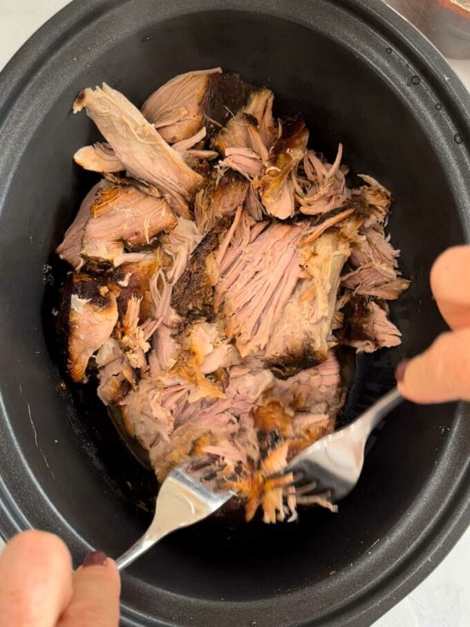 Step 3 in the recipe for Slow Cooker Pulled Pork. Pull apart meat after 12 hours of cooking with two forks.