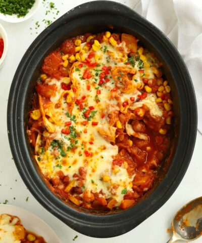 Slow cooker pot filled with veggie enchiladas, cooked and topped with cheese.