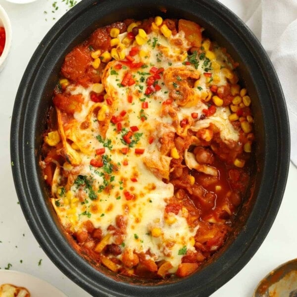 Slow cooker pot filled with veggie enchiladas, cooked and topped with cheese.