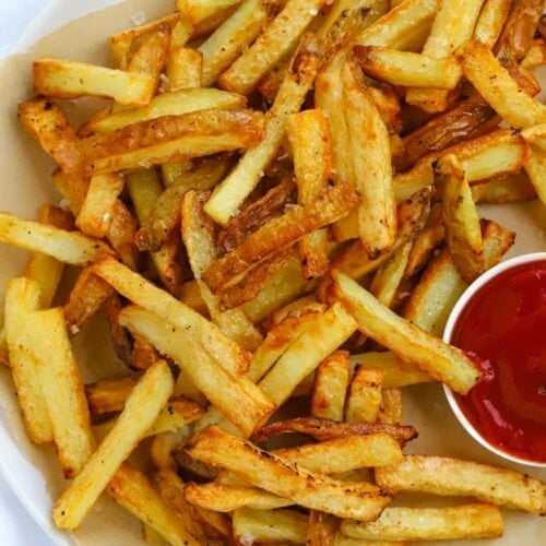 Homemade oven chips on a plate with ketchup in a side dish.