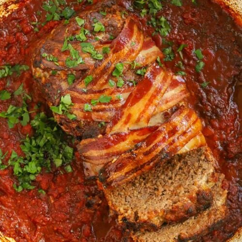 Delicious looking meatloaf out of the oven in a pot with sauce and bacon on top.