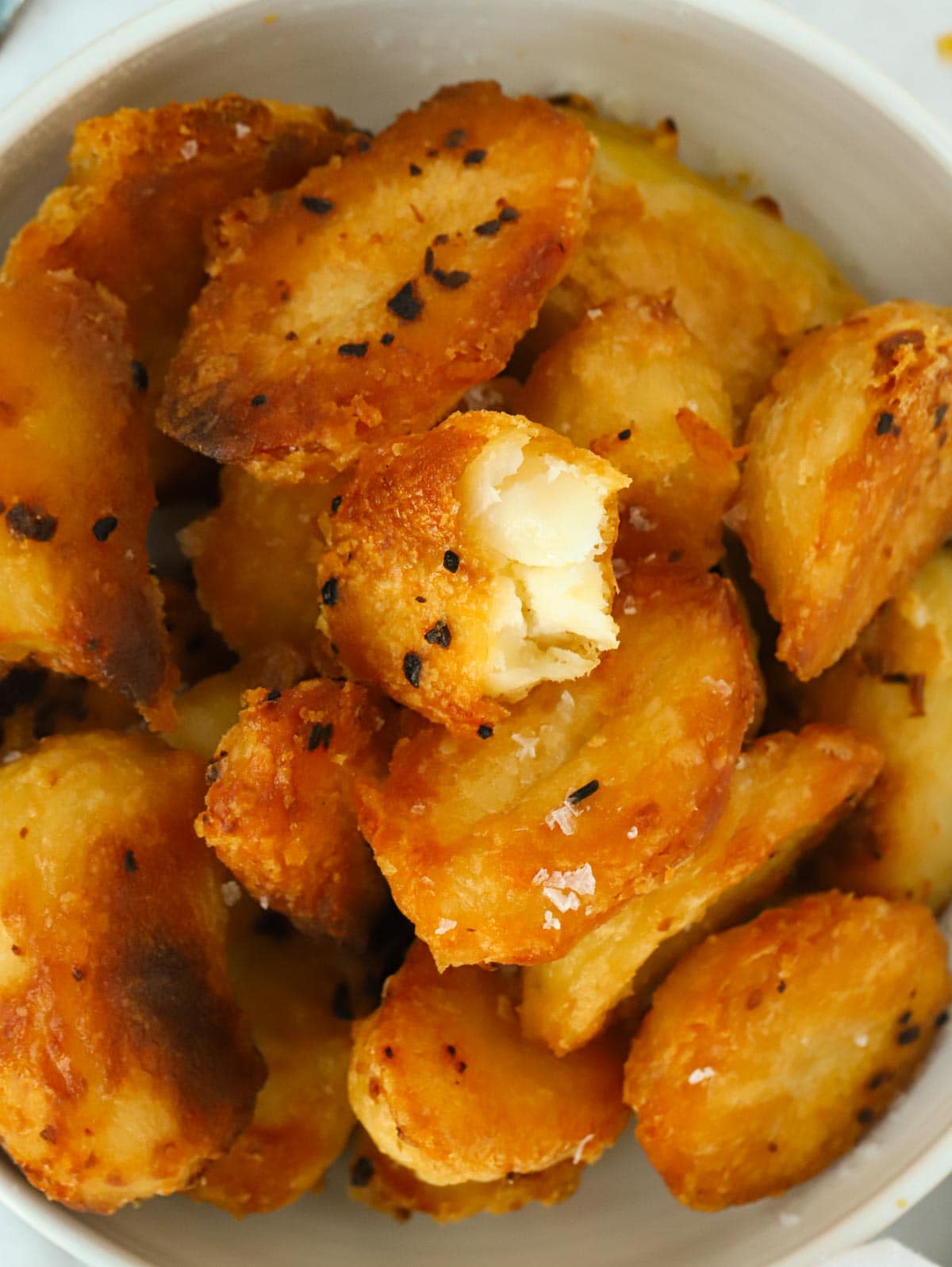 Big close up of a bowl of golden, crispy roast potatoes.