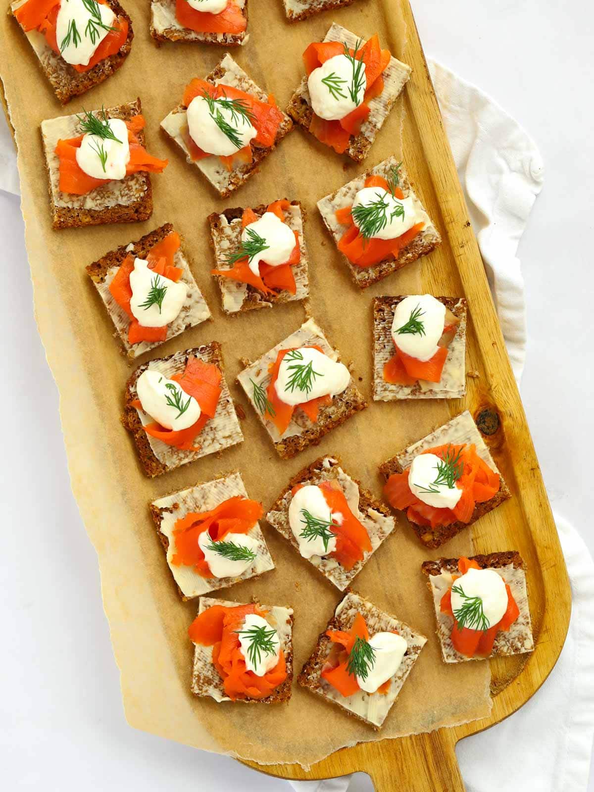 A serving board filled with squares of Smoked Salmon Canapés.