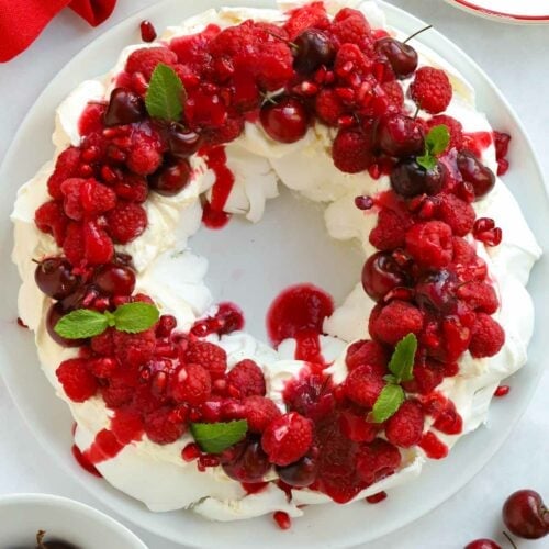A meringue dessert for Christmas looking like a wreath, with red berries and sprigs of mint.